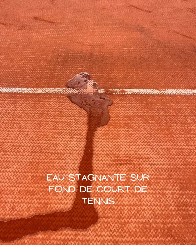 Eau stagnante sur le fond d'un court de tennis abîmé signalant un défaut de drainage