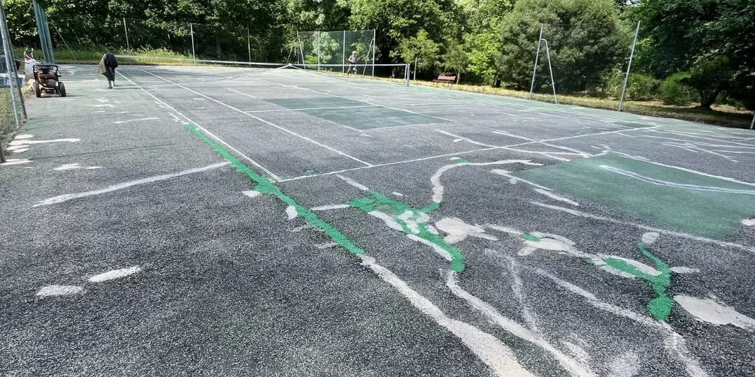 Fissures traversant un court de tennis en enrobé nécessitant un rebouchage avant rénovation